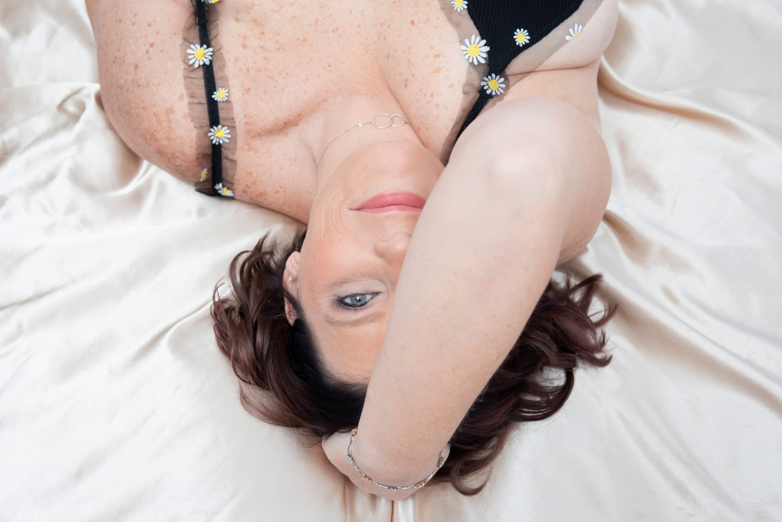 A woman covers half her face with her arm while looking into the camera during her boudoir photo shoot.